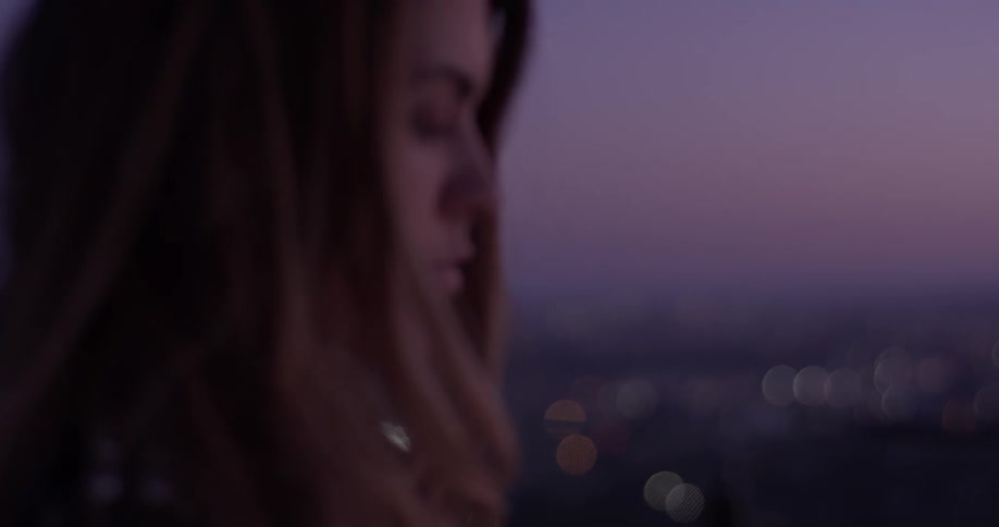 A woman stands high above a city as the sun sets