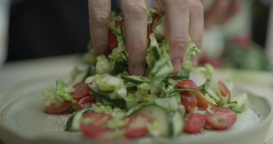Hand places salad on a plate