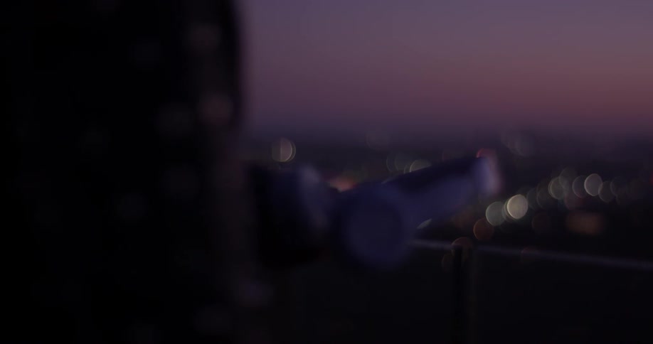 A person's hands hold a set of headphones while looking out over the night lights of a city