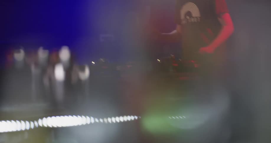 A man at a club does a dj performance on stage with red and blue lights shining on him