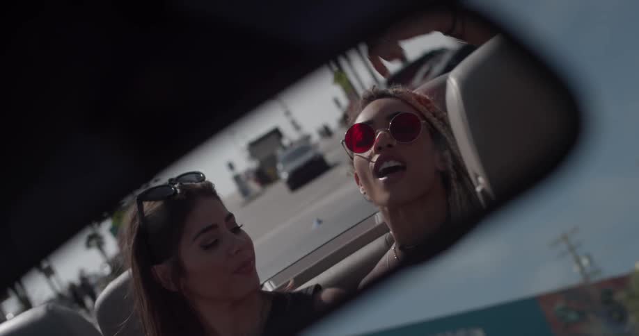 Two women dancing in the back of a convertible driving down the road