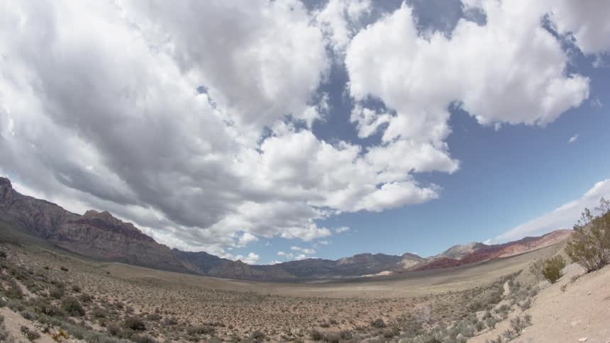White fluffy clouds roll in along flatlands with mountains in background
