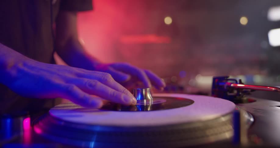 A dj changing out a record on a turntable, then he turns the record by hand