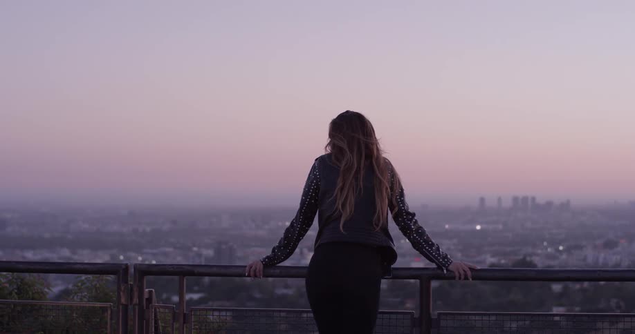 Woman leans on a railing looking at the city below