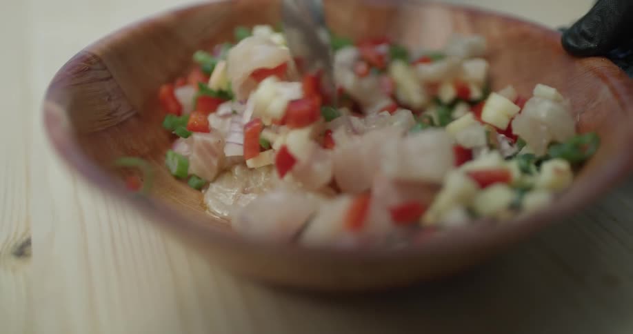 Someone stirs a garden salsa in a wooden bowl