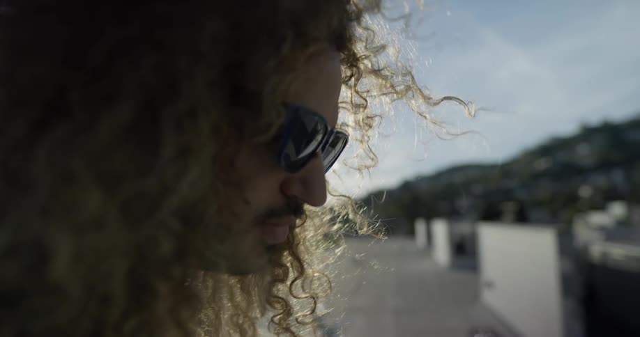 A male with sunglasses on a rooftop nodding his head