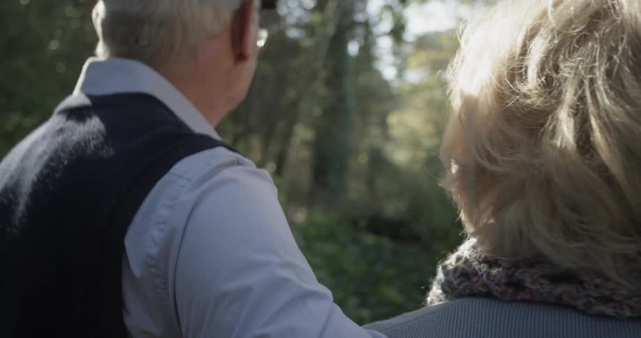An elderly man walking with his arm around a woman in the woods