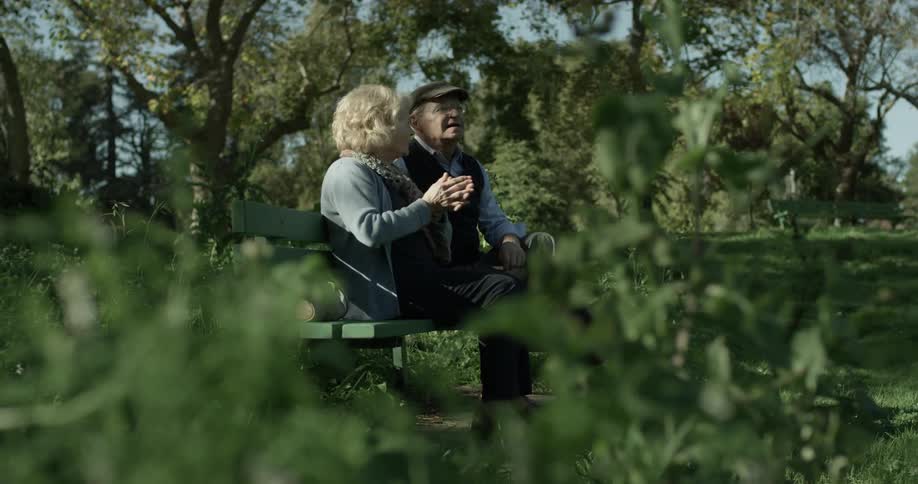 An older couple sit on a bench as they talk and look at the scenery