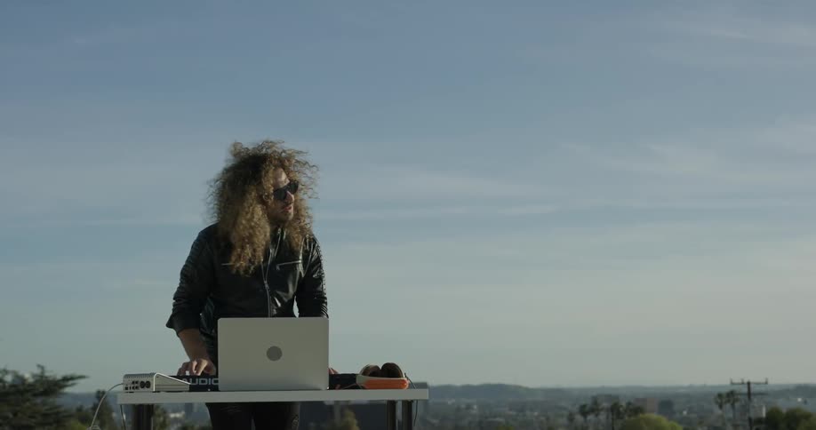 Dj playing music outdoors at a table in front of blue sky