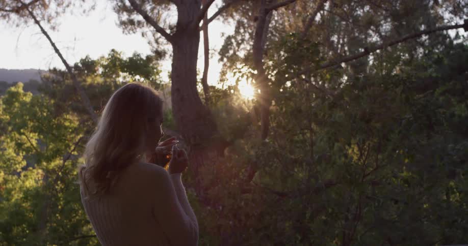 The top part of a woman standing and looking into the woods while drinking a cup of tea