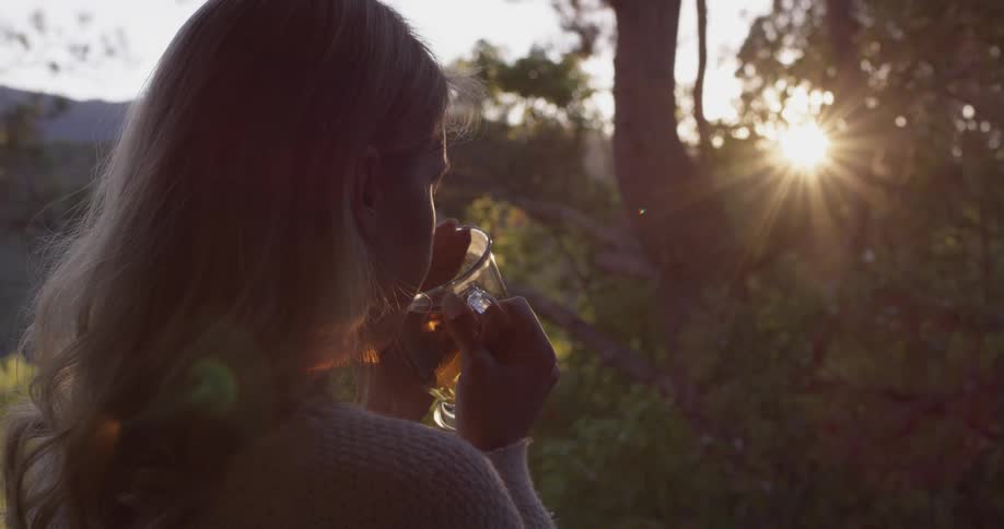 Closeup of a woman enjoying a cup of tea and staring at the sun between some trees