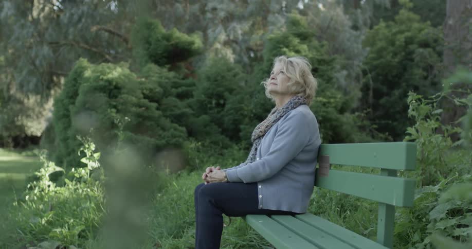 Older woman sits on a bench looking around