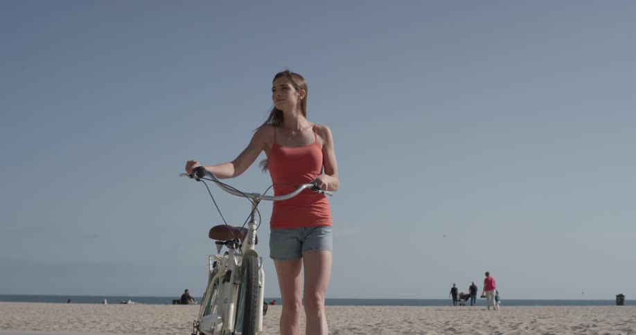A woman walks her bike along a path on a beach