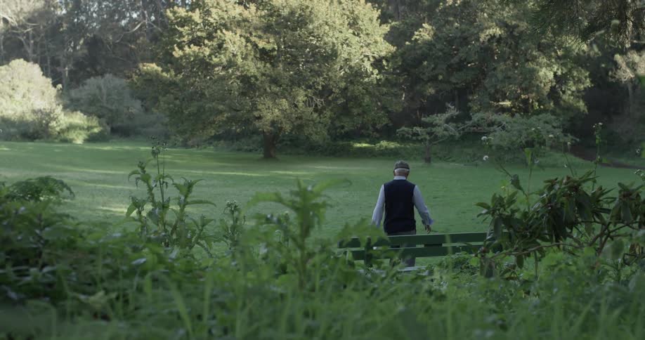 A man walks casually away from a bench at the park on a sunny day