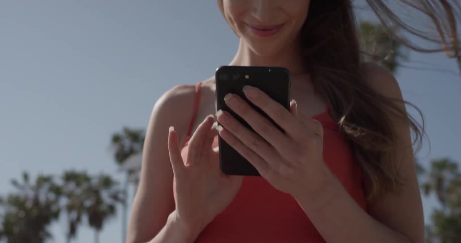 Woman stands outside on a sunny day smiling at looking at her phone