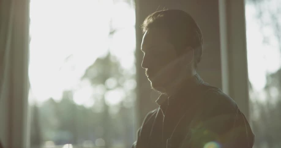 A man sits in front of a window playing a piano