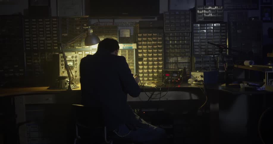 Man solders under lamp light at a workbench