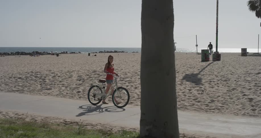 A woman walks her bike near the beach