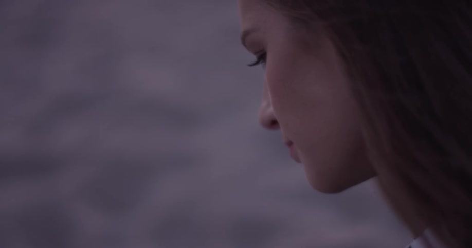 A woman on the beach looks down at her phone at dusk