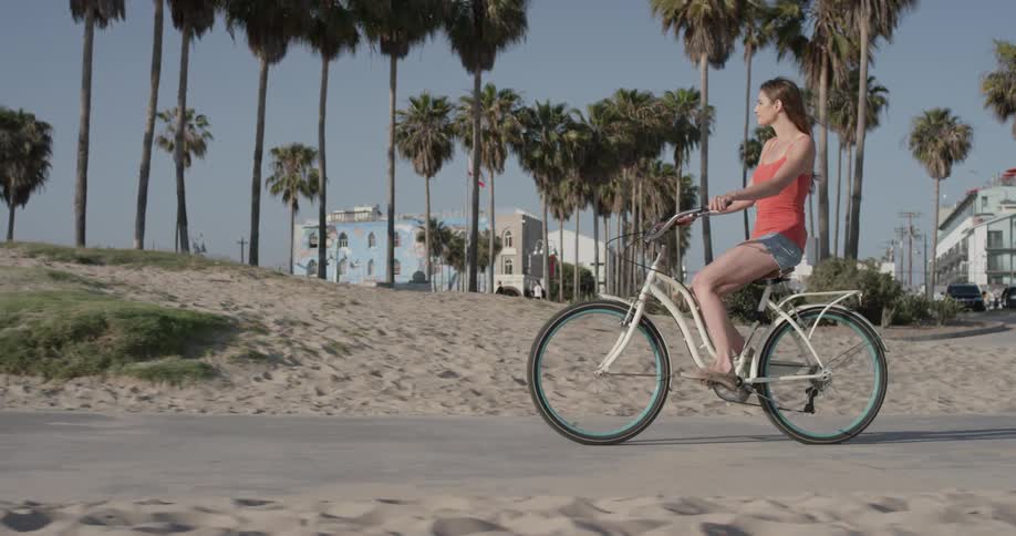 A woman rides a bike on a path cutting through the sand of a beach