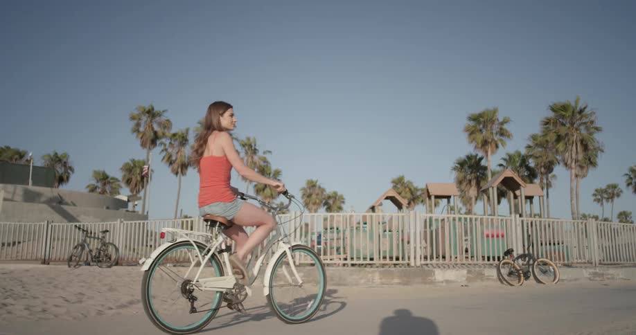 Woman riding a bike down a sidewalk at the beach with a playground in the background
