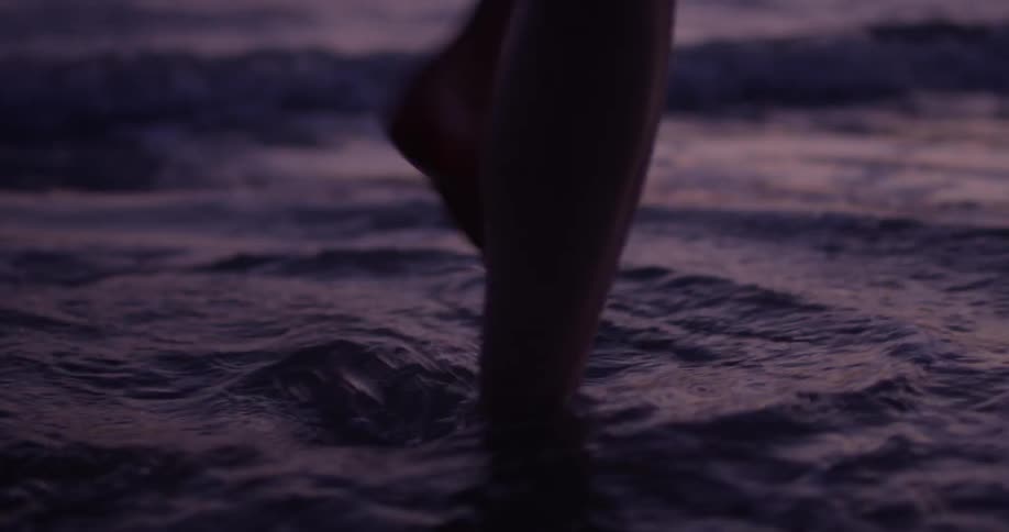 A woman walks on the beach while waves lap at her feet