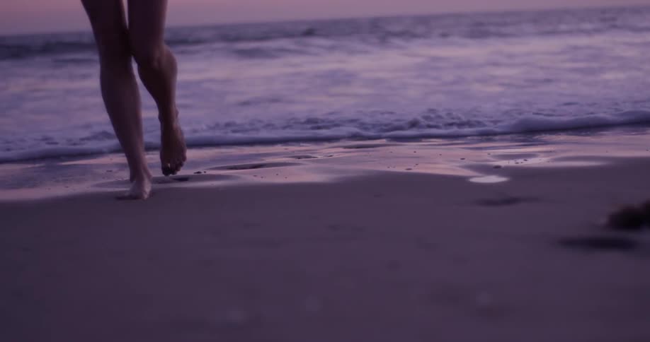 A woman walking on the beach at sunset
