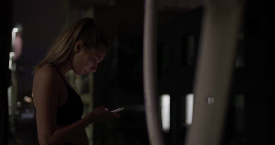 The upper half of a woman in a sports bra looking at her smartphone