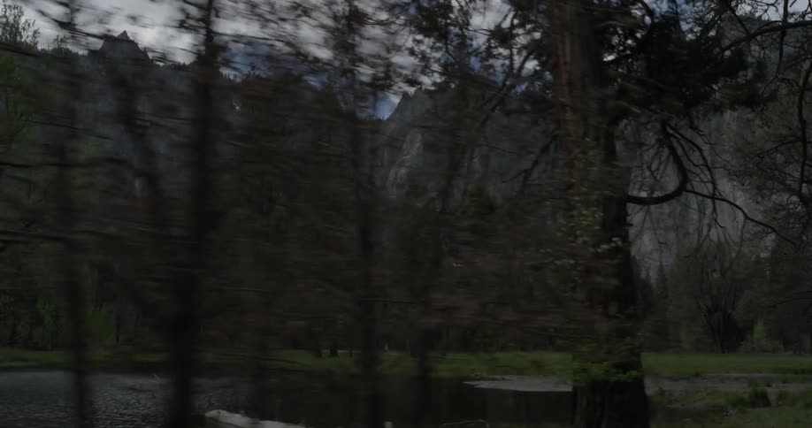 Flying by or driving by a beautiful forest with a river and mountains in the background on a sunny cloudy day