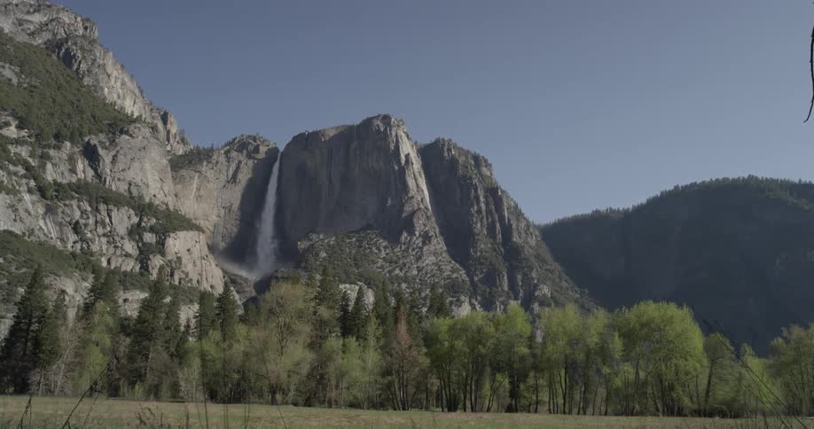 A beautiful landscape of mountains and waterfalls adorned with trees and a grassy field