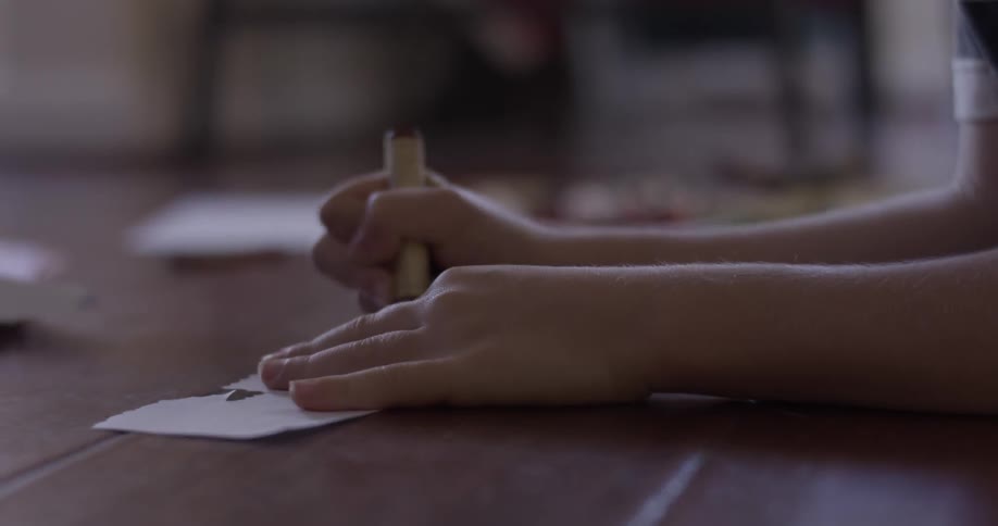 A boy uses a thick crayon to draw on some scraps of paper on the floor