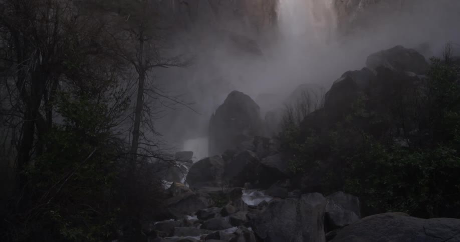 A dark lit waterfall with rocks and trees surrounding the waterfall