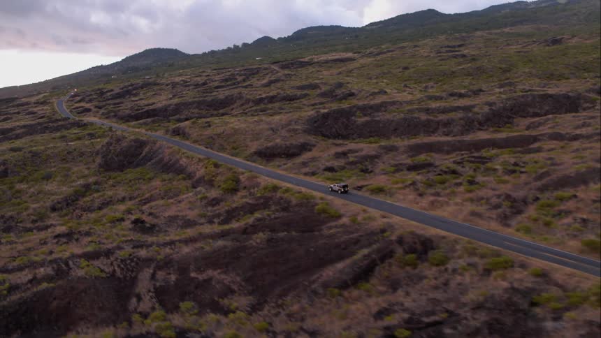 A car drives down a long straight road with mountains in the distance