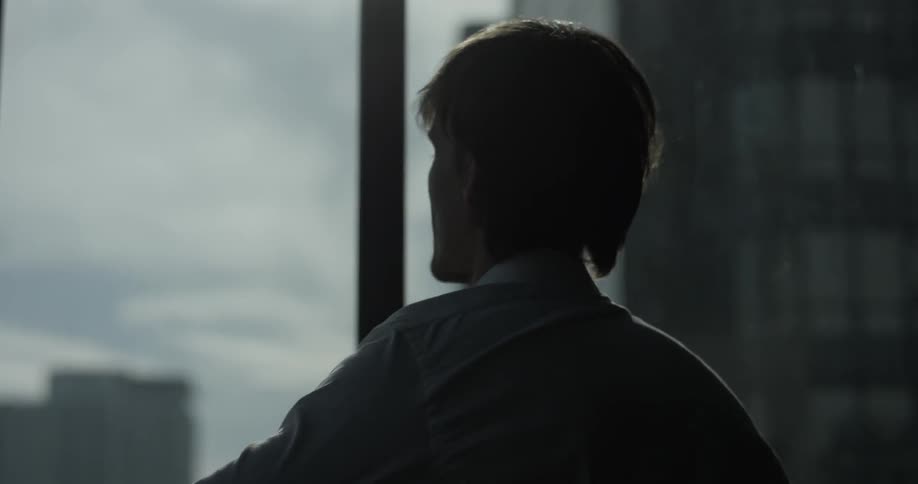 Man looks out the window while putting on a shirt