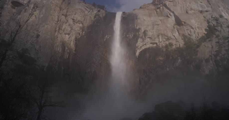 Water falls off of a waterfall into the valley below generating mist and rain droplets for the trees below