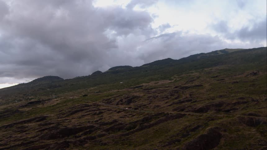 Mountain with dark clouds in the background, with car driving down mountain road in distance