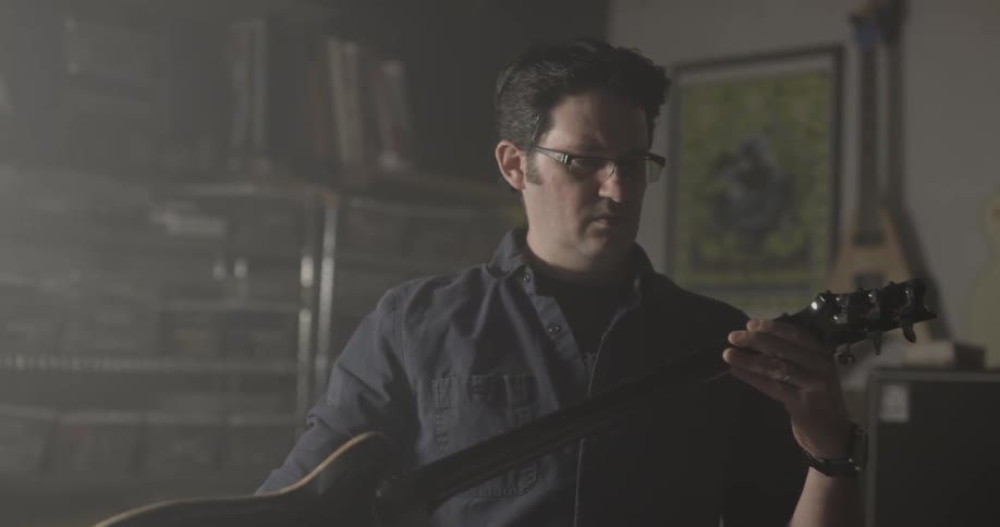 Man in glasses holds a guitar then sets it down on a table
