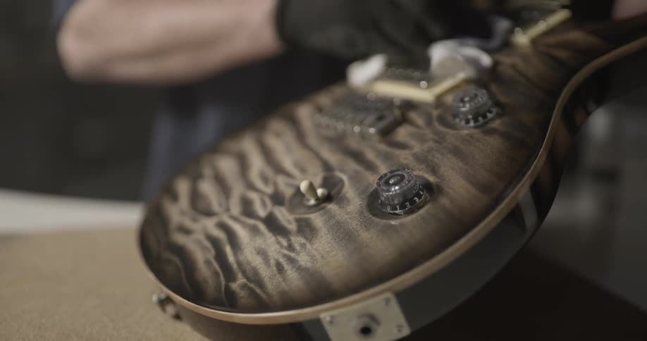 A man wearing gloves wipes an electric guitar with a cloth