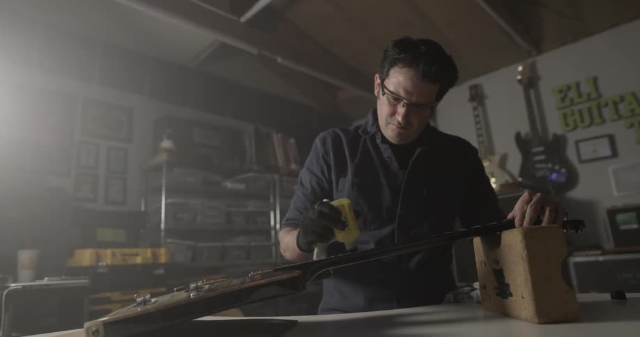 Man applies yellow liquid in bottle on a guitar neck