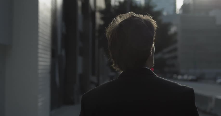A man in a suit strolls down the sidewalk of a major city with tall buildings around him
