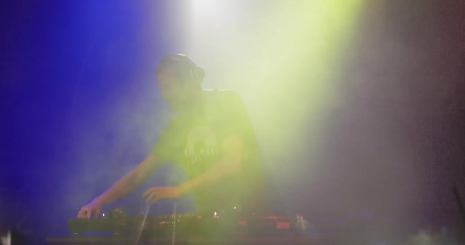 A dj mixes while lights strobe over him