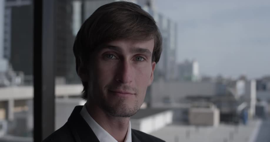 A man turns to look at the camera with a slight smile on his face and continues to stare for a bit
