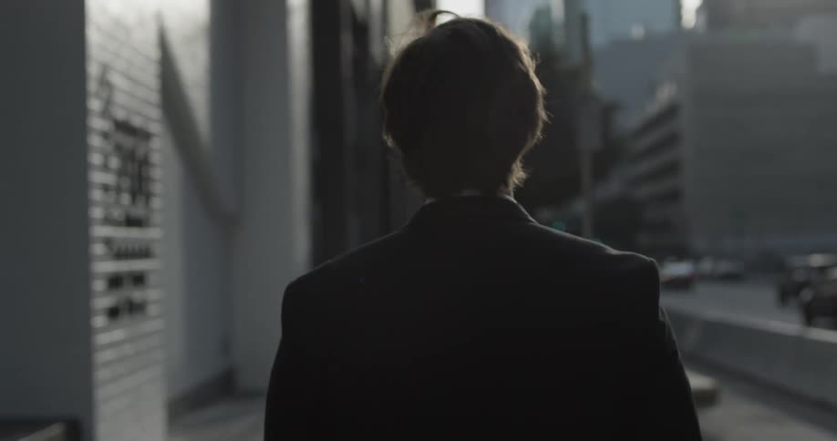 Man walks through a busy city on the sidewalk wearing a suit and passes a garage while the sun is setting