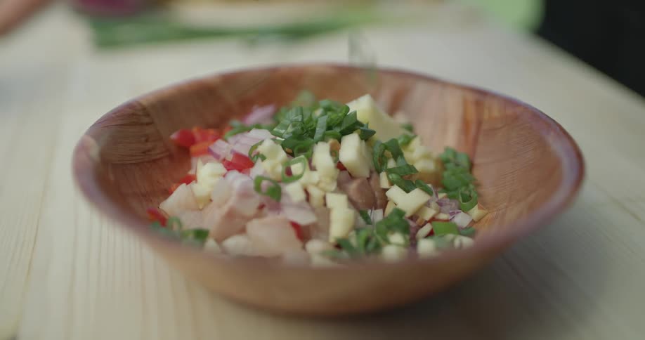 Food inside a wooden bowl is topped off with freshly cut chives