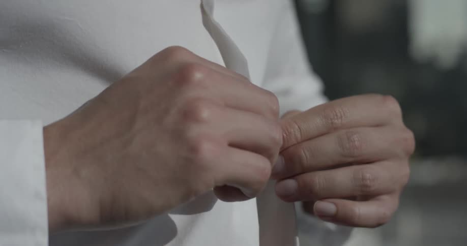 A man buttons his white shirt while standing with bright sunlight shining on to him