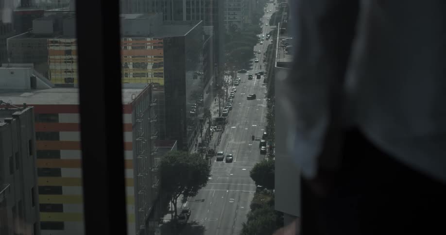 Man looks out high rise window at traffic below