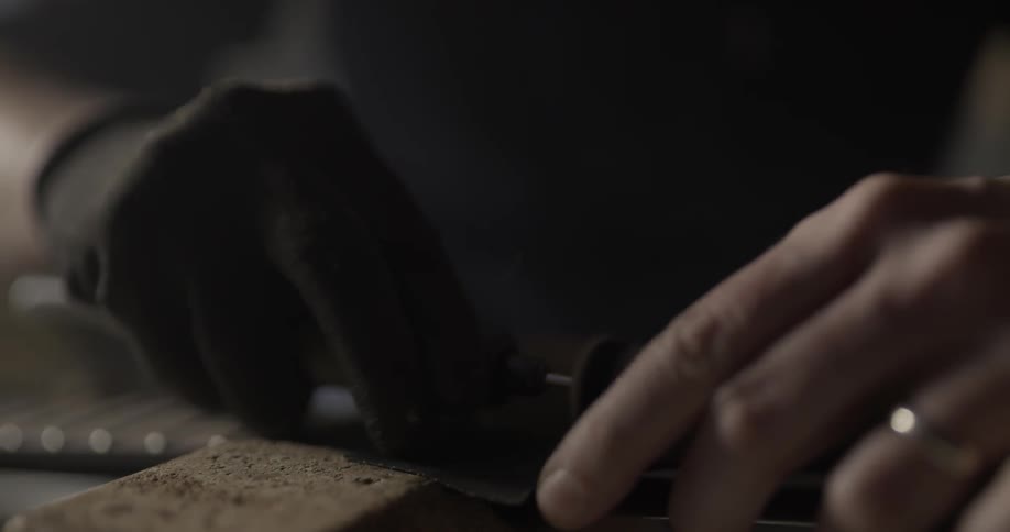 Person uses a tool on a guitar while wearing a glove