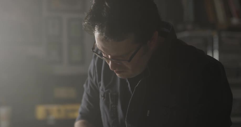 Man with glasses looking down and cutting in a room