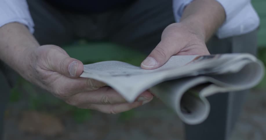 Old man is holding a newspaper and sitting on a bench at the park