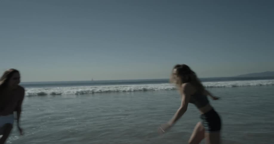 Two women run on shore line and splash each other